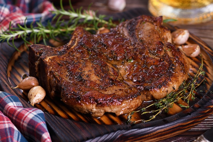 Photo roasted  pork chop on the bone steak
the meat is served on a wooden plate with rosemary