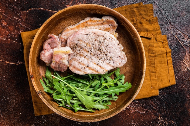 Roasted pork chop steaks or cutlets with arugula salad Dark background Top view