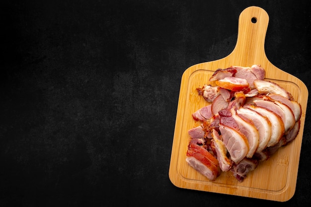 Photo roasted pork knuckle eisbein slice in wooden cutting board on dark tone texture background with copy space for text top table view flat lay german food pork leg