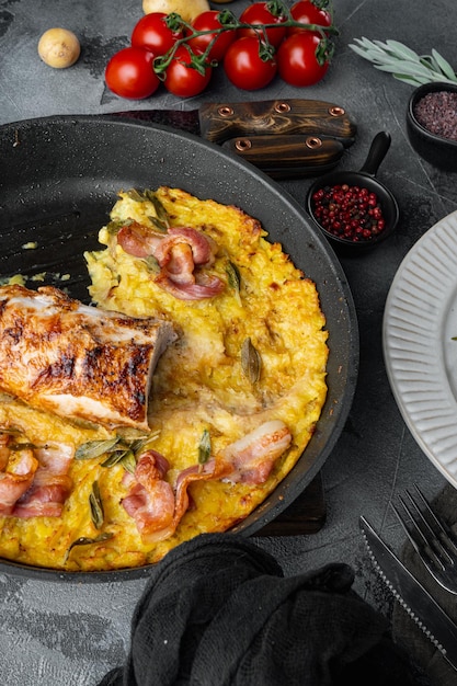 Roasted pork loin with mash potatoe gratin, sage and prosciutto set, on frying cast iron pan and plate, on gray stone background