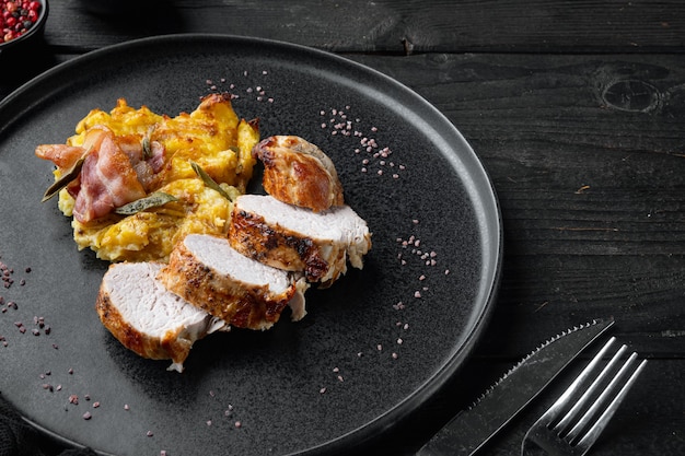 Roasted pork loin with mash potatoe gratin, sage and prosciutto set, on plate dish, on black wooden table background , with copyspace  and space for text