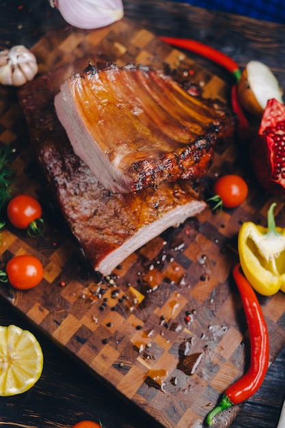 roasted pork ribs in a smokehouse standing on a cutting board garnished with rosemary pepper chili pepper tomato lemon pomegranate aromatic baked meat