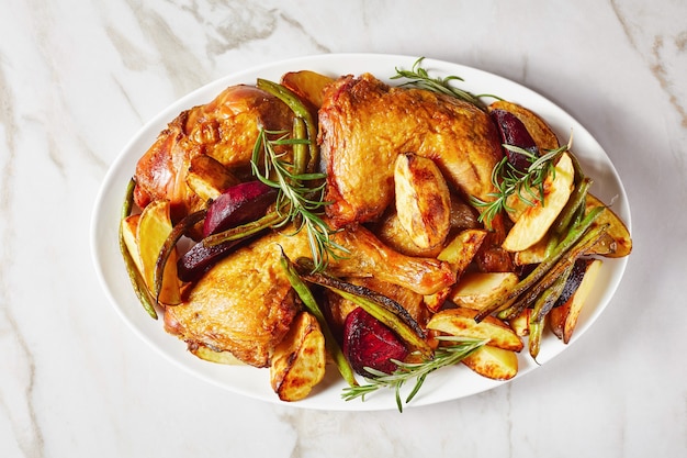 Roasted potato, beetroot, green bean and chicken legs served on a white oval plate on a marble table, horizontal view from above, flat lay