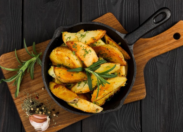 Patate arrosto con rosmarino fresco in padella di ghisa su fondo di legno nero vista dall'alto