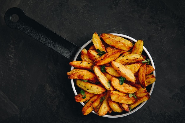 Roasted potatoes Baked potato wedges in frying pan on dark stone background