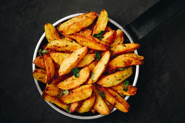 Roasted potatoes baked potato wedges in frying pan on dark\
stone background