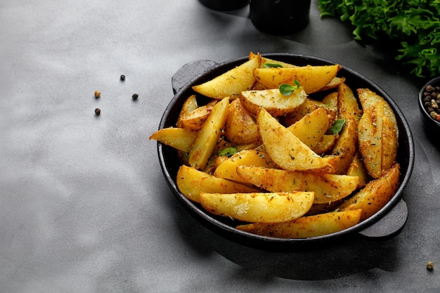 Roasted potatoes with herbs and spices Baked potato wedges in frying pan on dark stone background