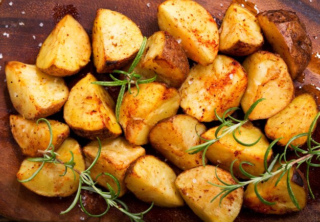 Roasted potatoes with rosemary on wooden board, top view