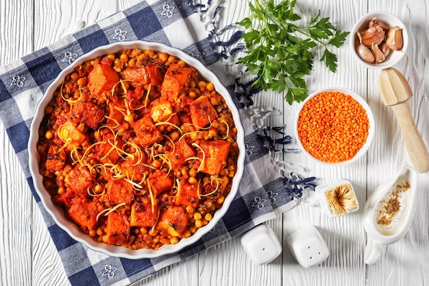 Roasted Pumpkin lentil chickpea dal in a bowl on a white wooden table with ingredients, horizontal view from above, indian cuisine, flat lay