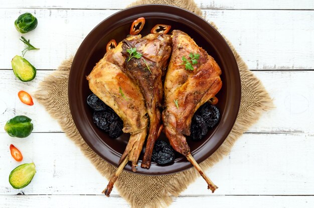 Roasted rabbit leg with prunes on a ceramic plate on light background