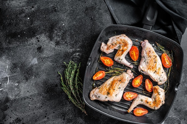 Roasted rabbit legs in a pan with thyme. Black background. Top view. Copy space.