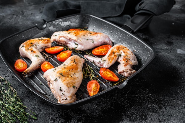 Roasted rabbit legs in a pan with thyme. Black background. Top view.