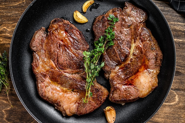 Roasted rib eye steaks  in a pan. Dark wooden background. Top view.