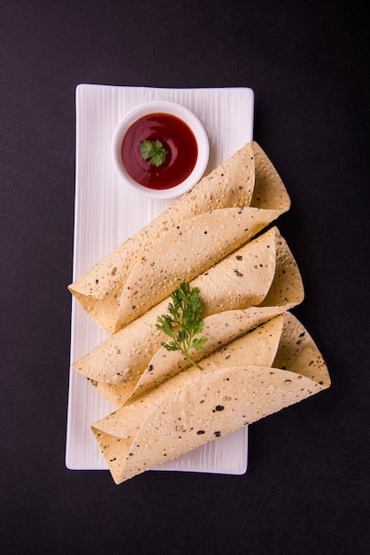 Roasted roll papad is een traditioneel Indiaas gerecht of bijgerecht, geserveerd met tomatenketchup op een kleurrijk of houten tafelblad. Selectieve focus