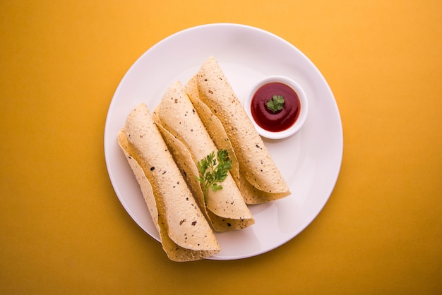 Roasted roll papad is een traditioneel Indiaas gerecht of bijgerecht, geserveerd met tomatenketchup op een kleurrijk of houten tafelblad. Selectieve focus