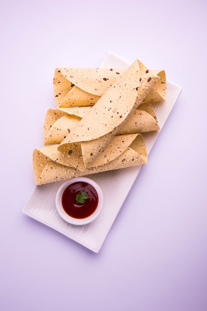 Roasted roll papad is an Indian traditional started food or side dish, served with tomato ketchup over colourful or wooden table top. Selective focus