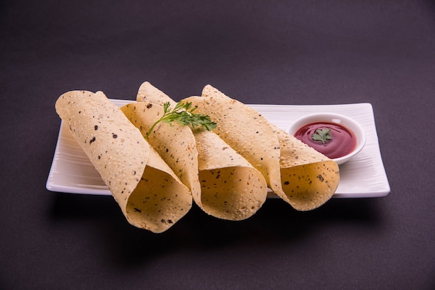 ローストロールパパドは、インドの伝統的なスターテッドフードまたはサイドディッシュで、カラフルなテーブルトップまたは木製のテーブルトップにトマトケチャップを添えて提供しています。セレクティブフォーカス