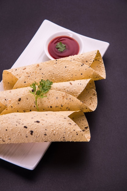 Roasted roll papad is an Indian traditional started food or side dish, served with tomato ketchup over colourful or wooden table top. Selective focus