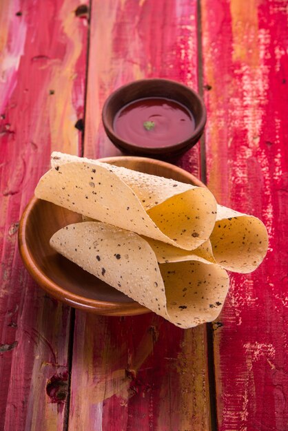 Roasted roll papad is an indian traditional started food or side dish, served with tomato ketchup over colourful or wooden table top. selective focus