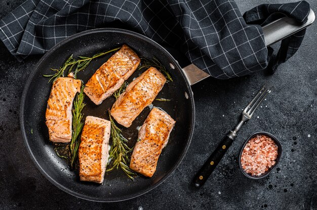 Photo roasted salmon fillet steak in a pan with rosemary. black background. top view.