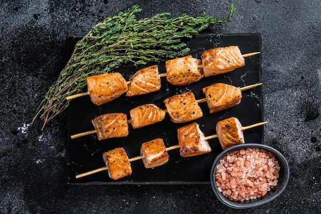 Roasted salmon kebab skewers on marble board. Black background. Top View.