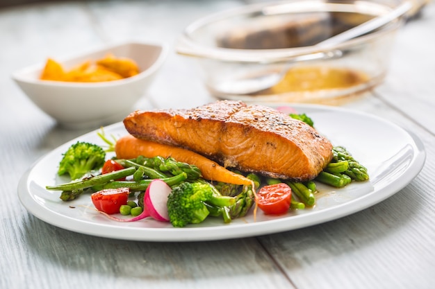 Trancio di salmone arrosto con asparagi broccoli carote pomodori ravanelli fagiolini e piselli