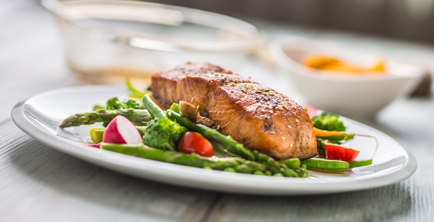 Trancio di salmone arrosto con asparagi broccoli carote pomodori ravanelli fagiolini e piselli