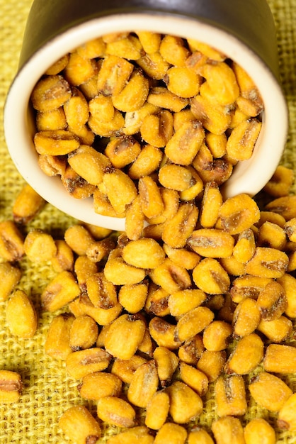 Roasted and salted corn in ceramic pot over yellow jute