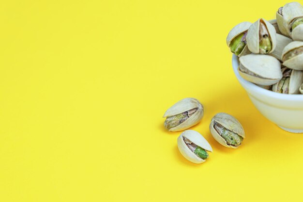 Roasted salted pistachios in a white ceramic bowl on a yellow background Closeup Popular beer snack Template for design space for text