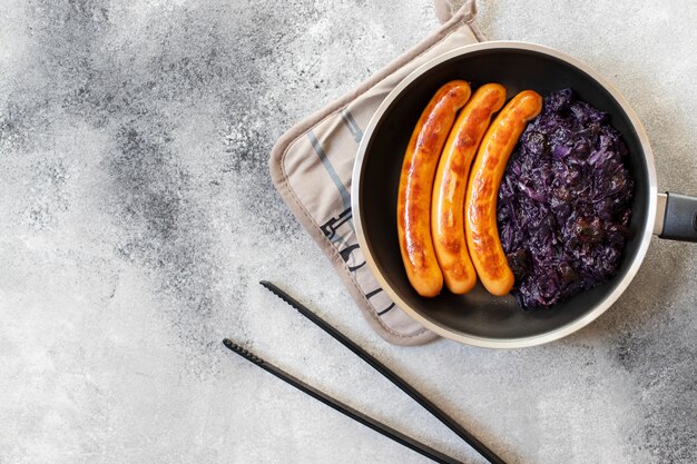 Roasted sausages bratwurst served in pan with bread and red cabbage on a gray background. Traditional German dish, German cuisine. Top view, copy space