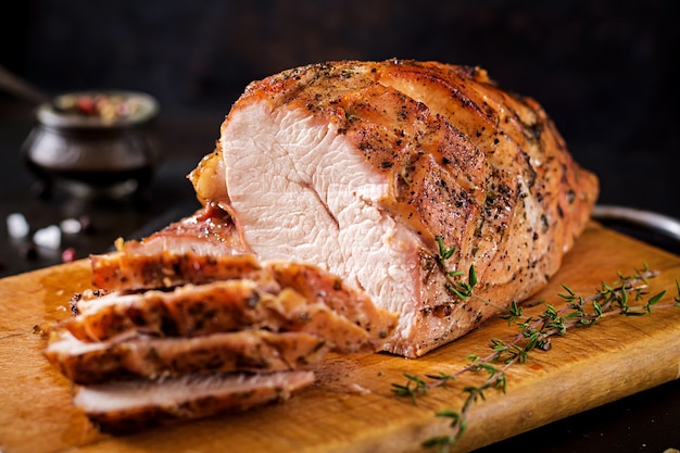 Roasted sliced Christmas ham of turkey on dark rustic background. Festival food.