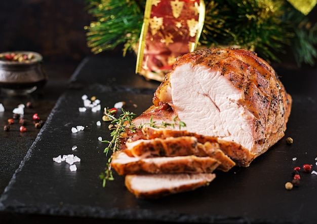 Roasted sliced Christmas ham of turkey on dark rustic surface. Festival food.