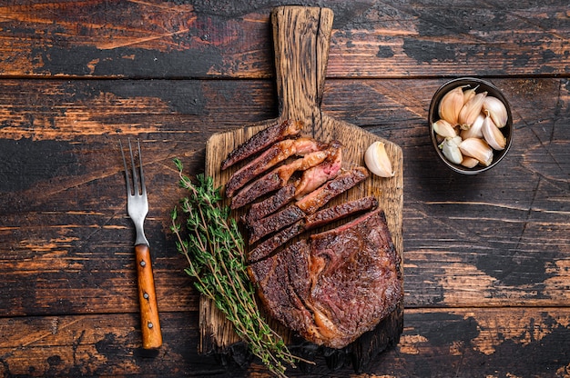 Roasted and sliced rib eye beef meat steak on a wooden cutting board with thyme.