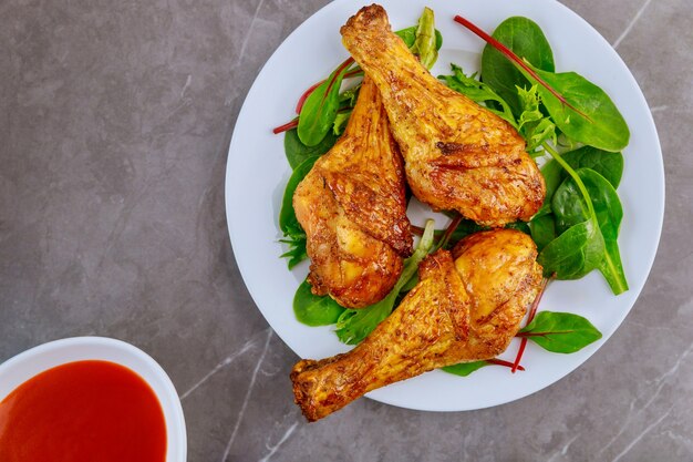 Roasted spicy chicken drumstick with salad and sauce on gray table. Top view..