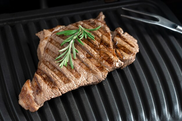 Roasted steak made of grainfed beef meat laying on grill decorated with fresh rosemary