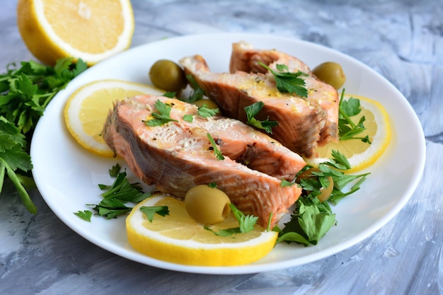 roasted steaks of salmon on white plate decorated with lemon, parsley and green olives