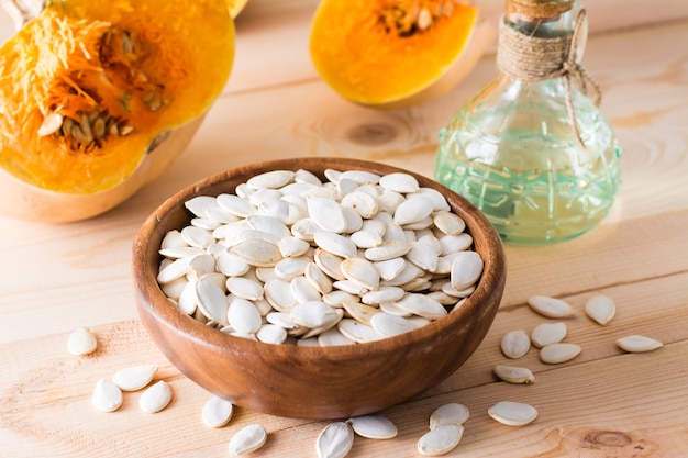 Roasted unpeeled pumpkin seeds in a plate, oil in a bottle and pumpkin pieces on a wooden table