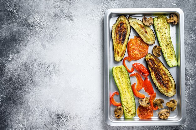 Roasted vegetables on a baking pan. White background. Top view. Copy space.