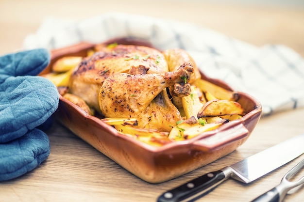 Roasted whole chicken with potatoes in baking dish. Tasty food at home on the kitchen counter.