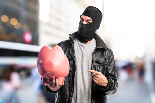 Photo robber holding a piggybank on unfocused background