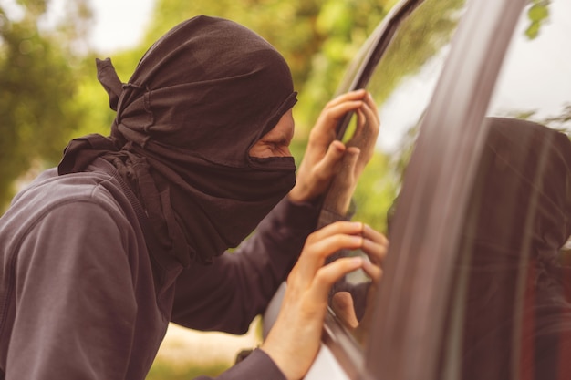 Robber standing next to the car and trying to steal things