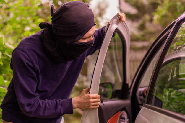 Robber standing next to the car and trying to steal things