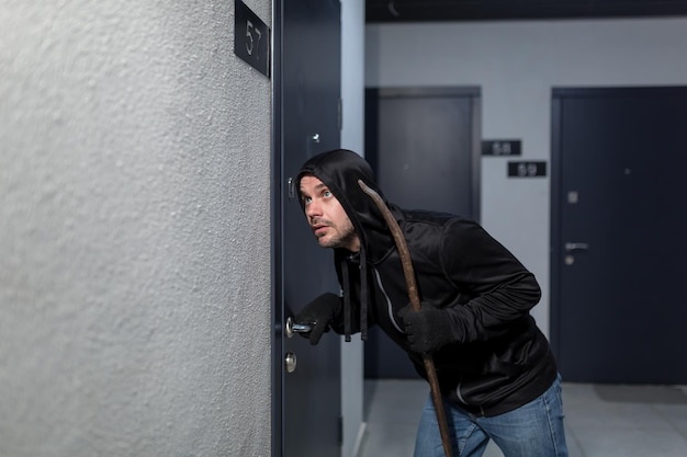 The robber tries to break the door lock in the apartment dressed in black