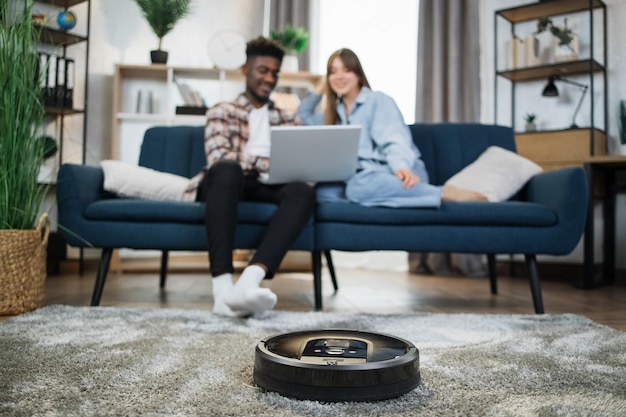 Robot cleaning apartment while couple relaxing on couch