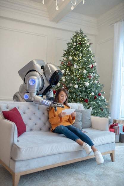 Robot and a cute girl sitting on the sofa spending time together