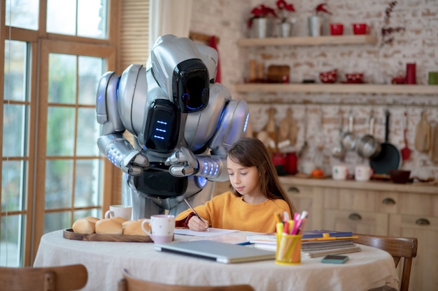 Учитель-робот внимательно смотрит, как девочка пишет