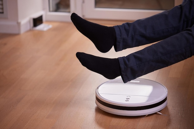 Robotic vacuum cleaner cleaning the room while man sitting on sofa