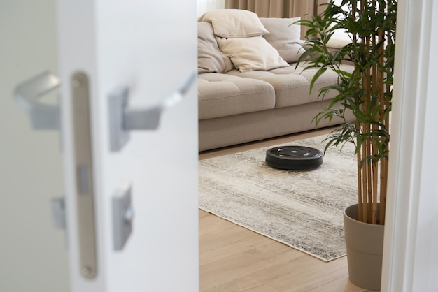 Robotic vacuum cleaner on the floor in cozy modern living room, view through open door