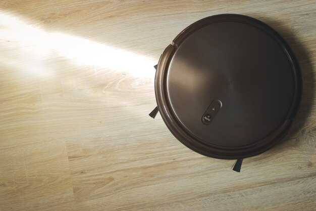 Robotic vacuum cleaner on laminate floor in action. housework and technology concept.