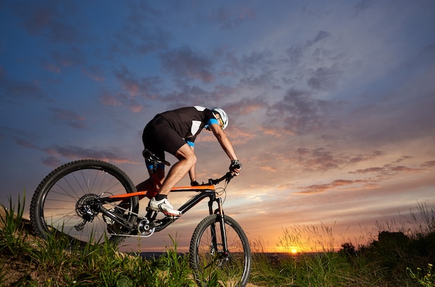 Robust and sporty man sitting on bicycle and cycling. Energetic cyclist riding bike on trail with grass